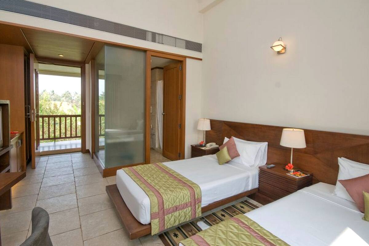 A hotel room with two beds, a balcony, a sliding door, and a small bedside table with a lamp.
