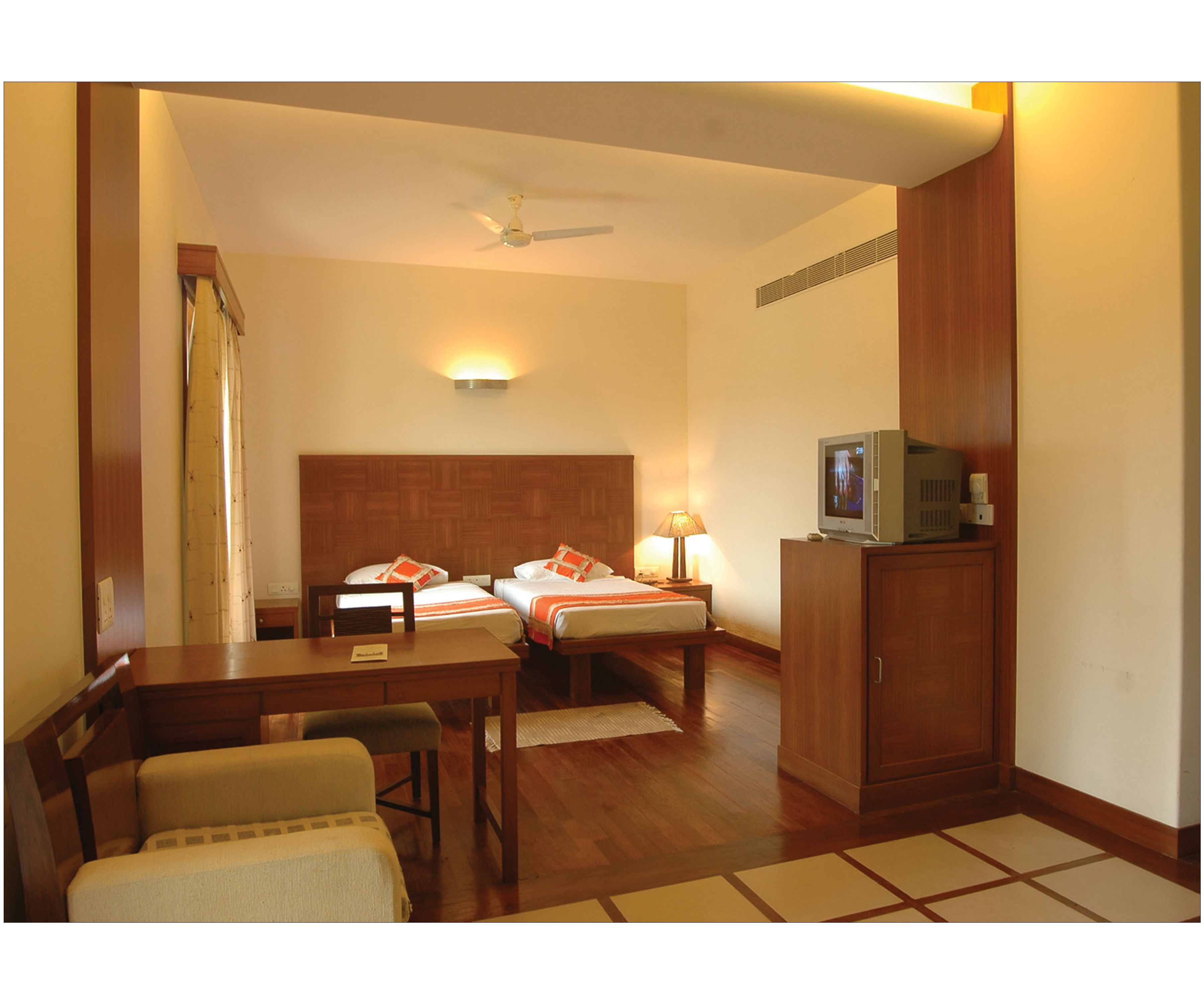 A hotel room with two beds, a desk, a chair, a television, and a ceiling fan.
