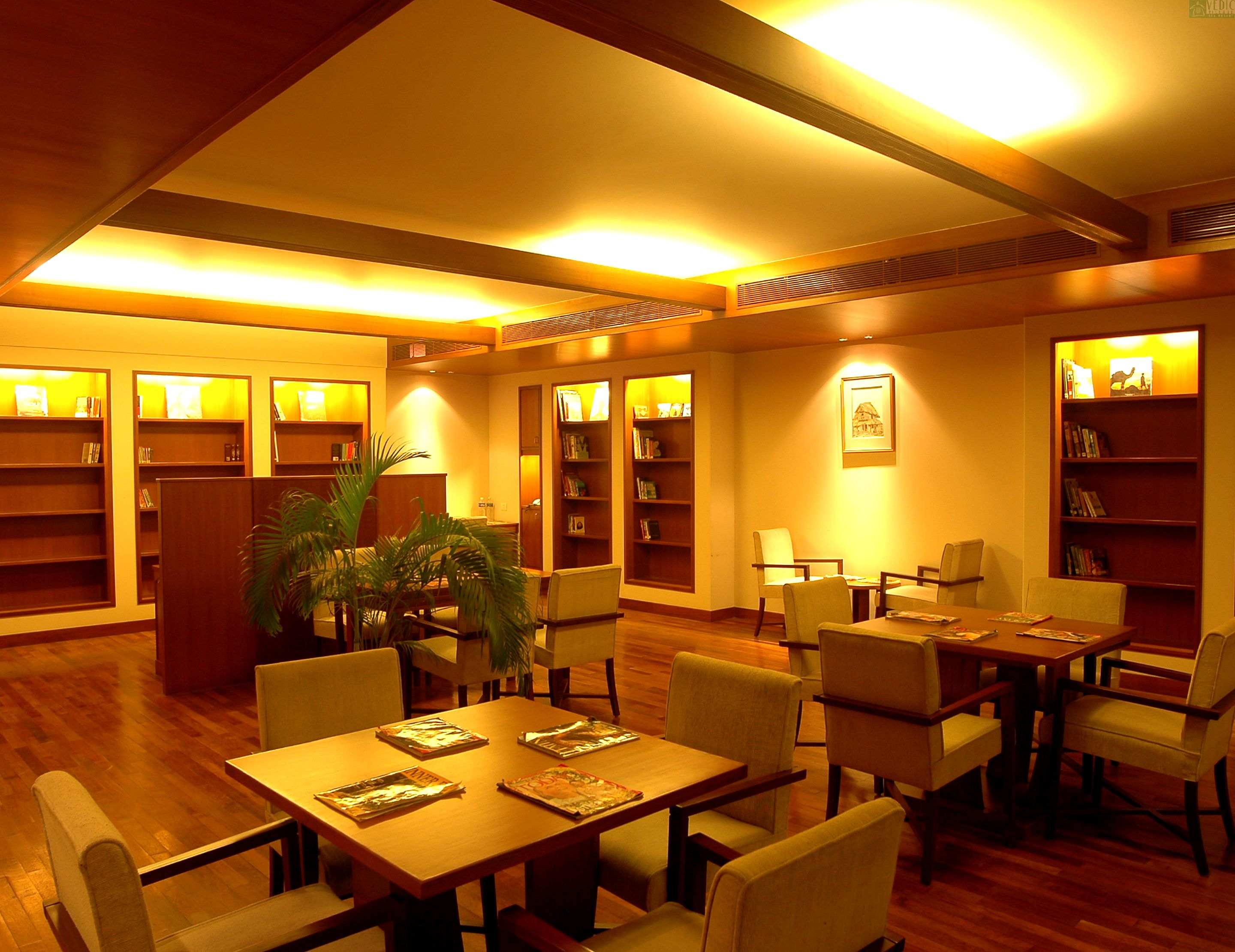 Una biblioteca con estanterías de madera, una mesa central con sillas y una planta en maceta.