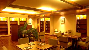 Una biblioteca con estanterías de madera, una mesa central con sillas y una planta en maceta.