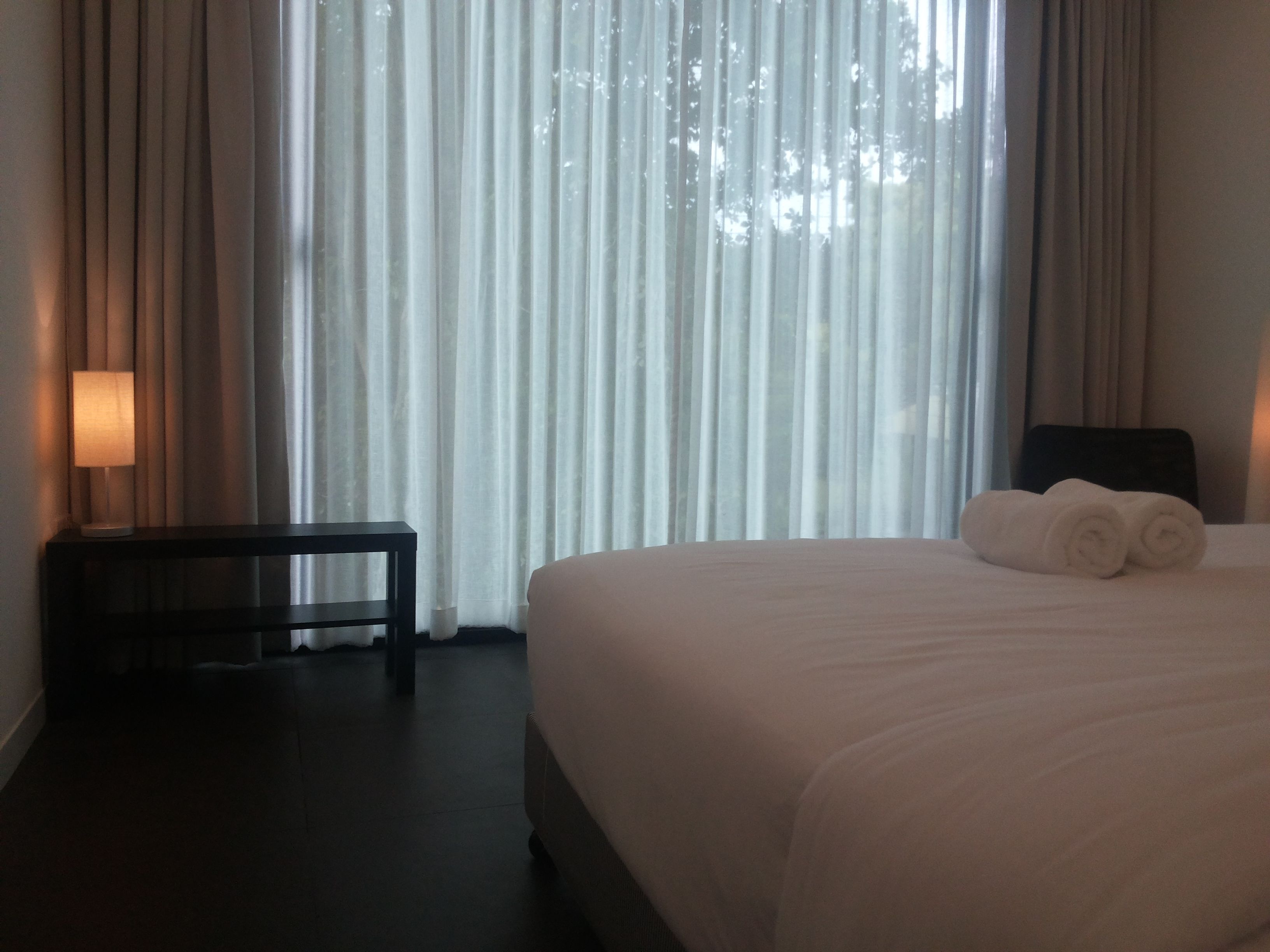 A hotel room with a large bed, a bedside table, and a lamp.
