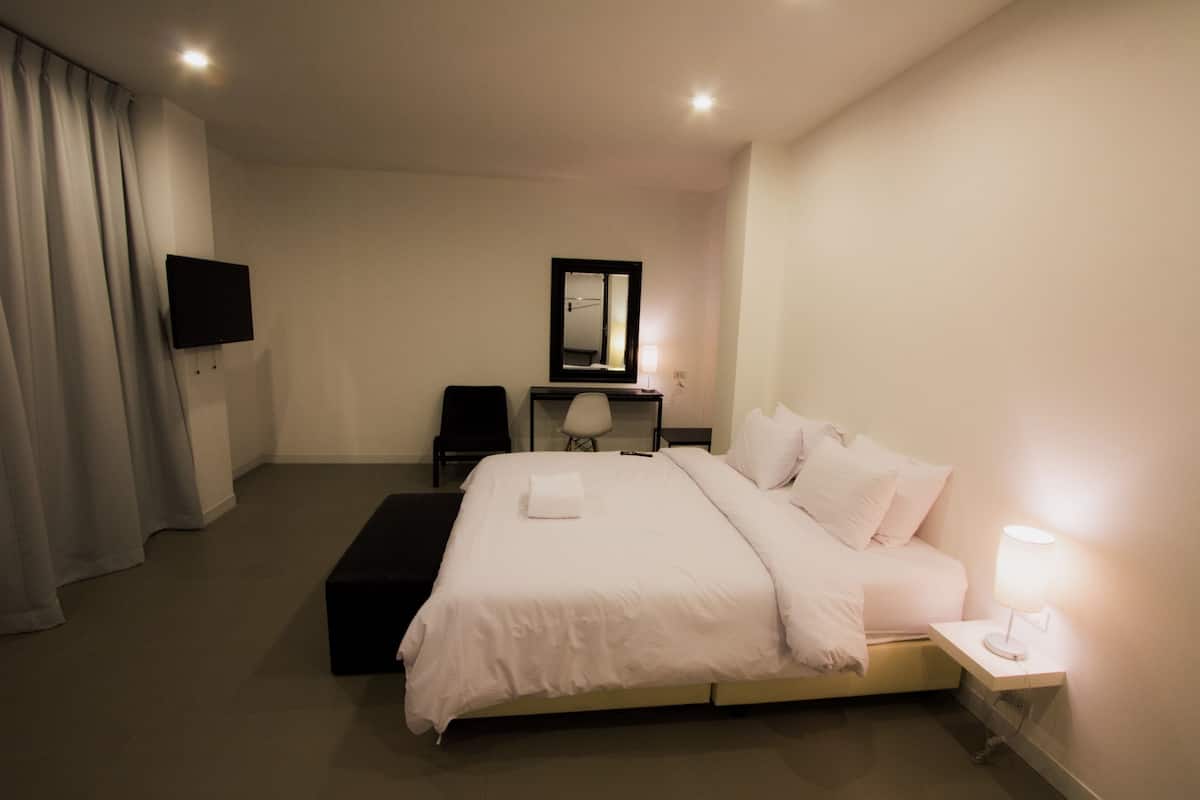 A hotel room with a bed, bedside table, lamp, chair, desk, TV, and a mirror.