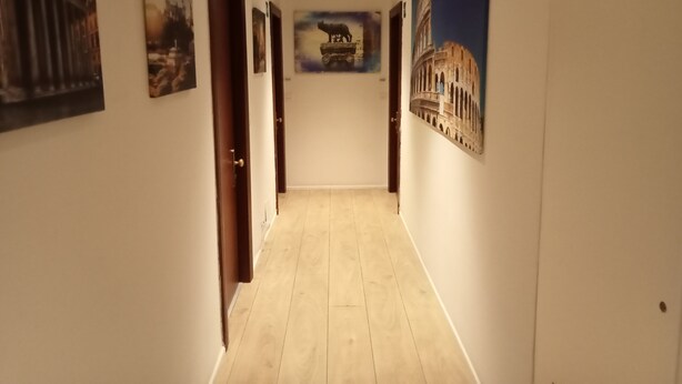 A hallway with wooden flooring, white walls, and various framed pictures including a coliseum. - Why Not Roma (Rome)