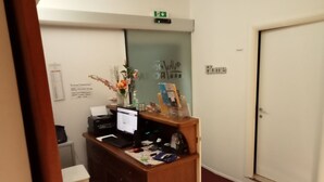 A reception desk with a computer, a printer, and a small desk lamp. There is a chair in front of the desk and a door to the right. - Why Not Roma (Rome)