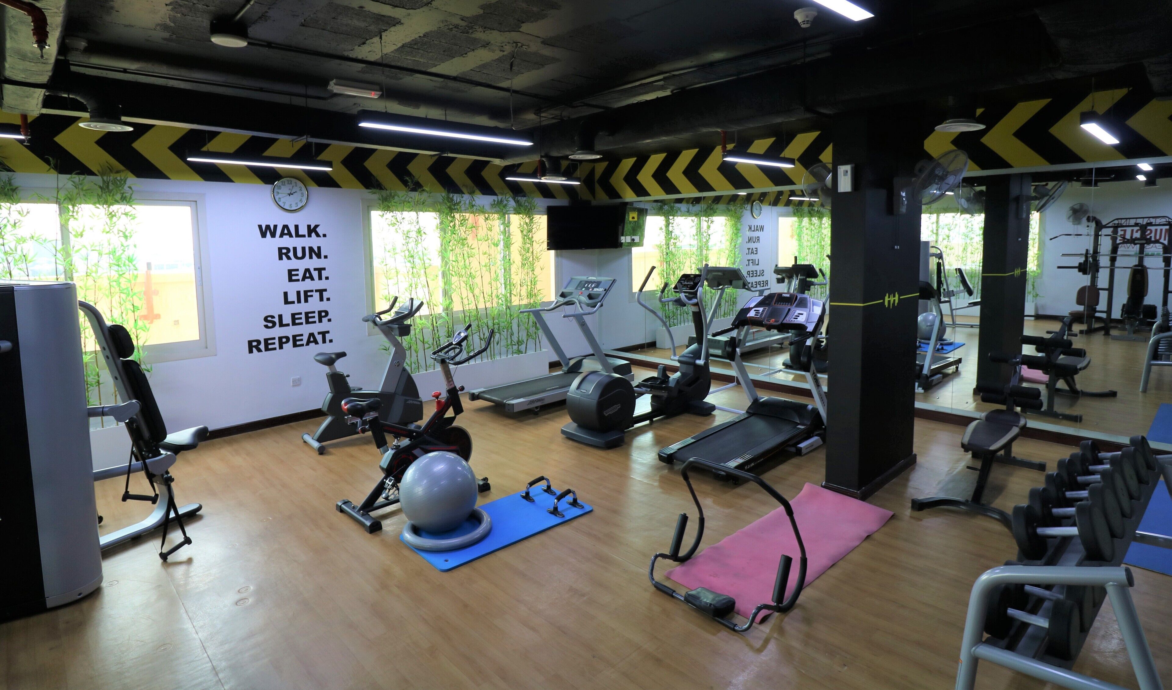 Une salle de sport équipée de divers appareils d’exercice, un mur orné de citations motivantes et de grandes fenêtres laissant entrer la lumière naturelle.