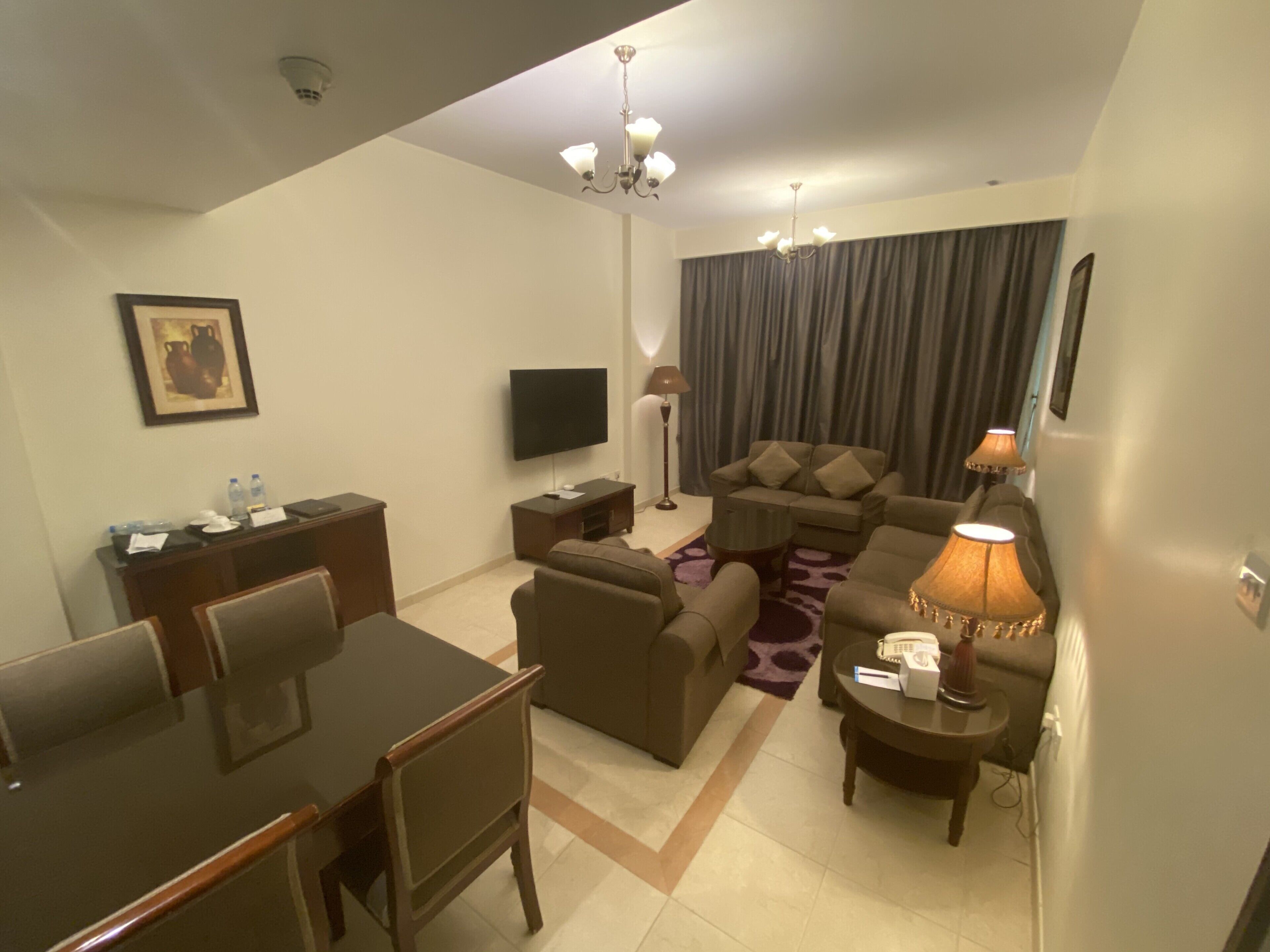 A modern living room with a flat-screen TV, sofa set, dining table, and chairs.