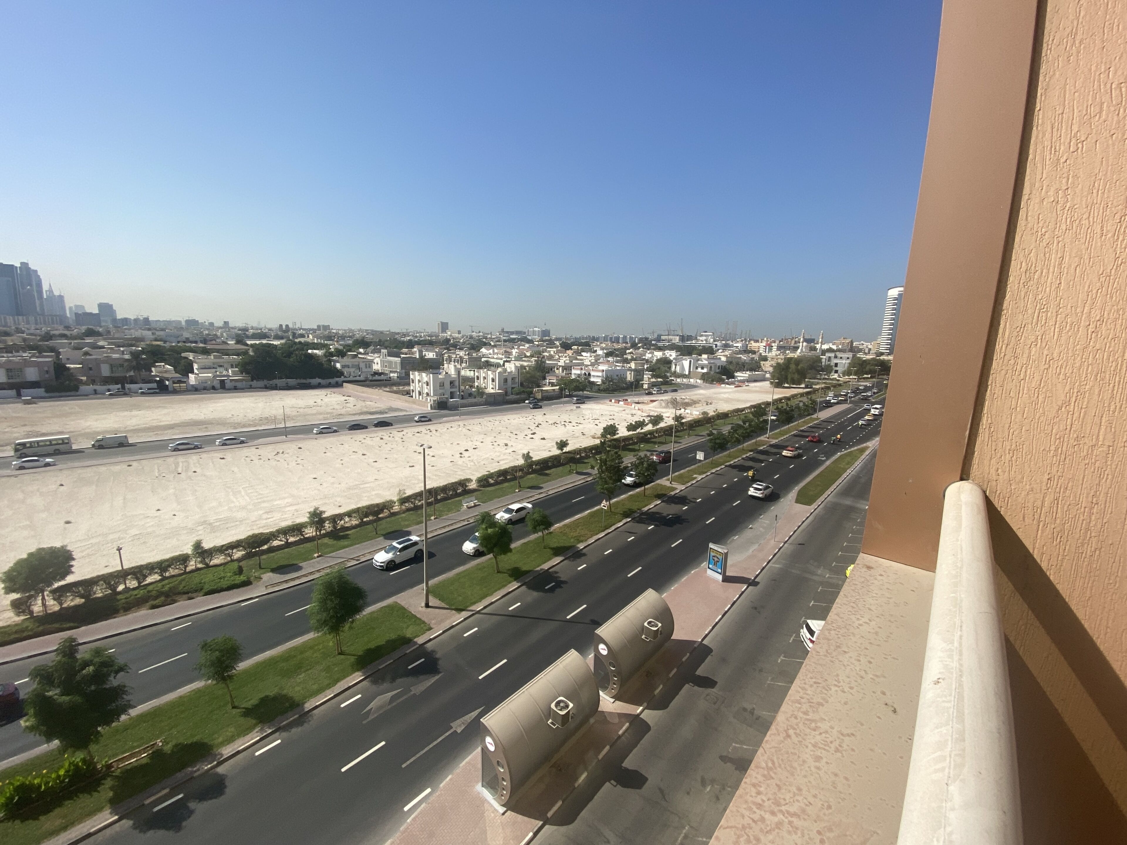 A view from a balcony overlooking a cityscape with multiple roads, buildings, and a clear sky.