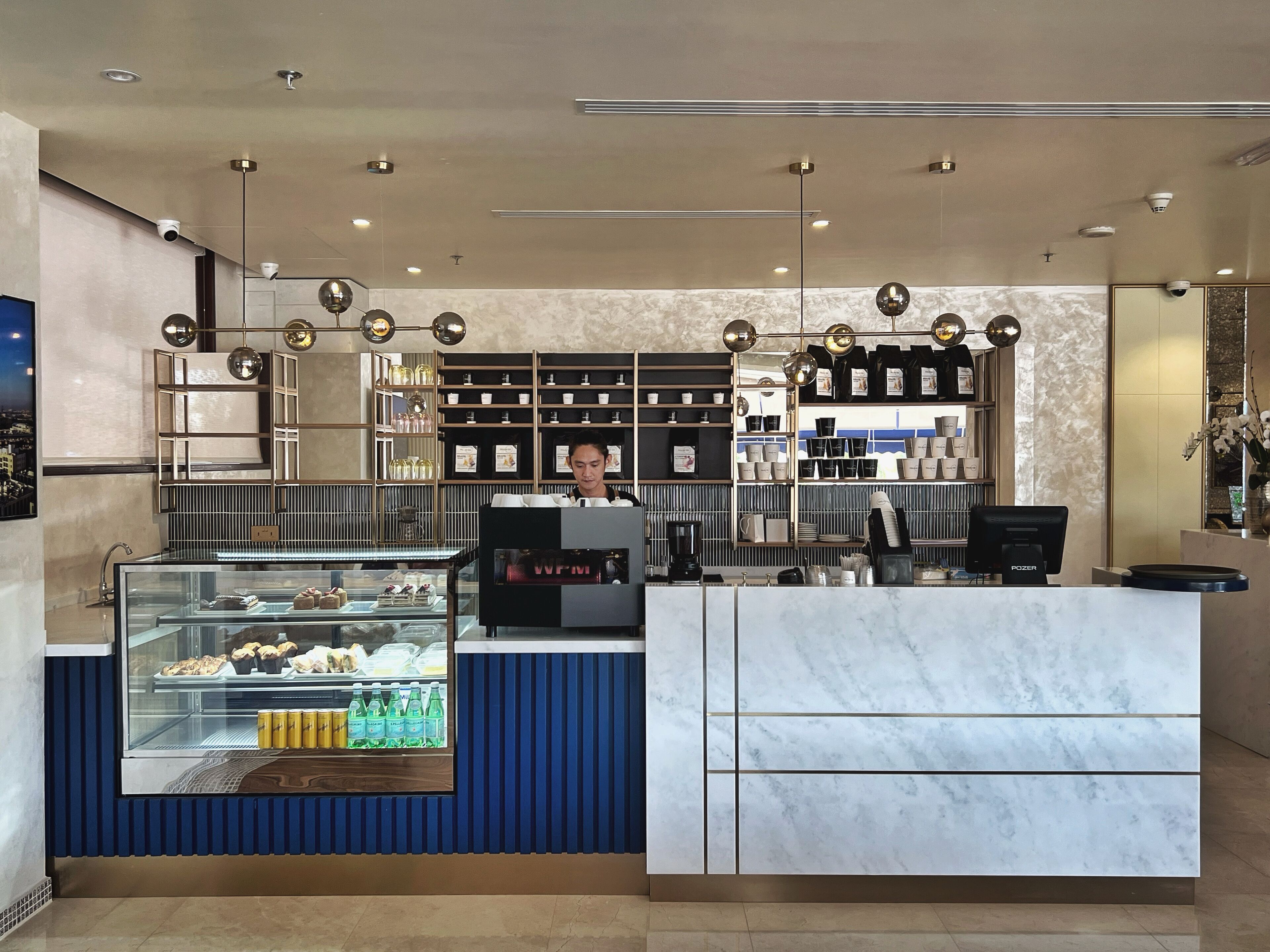 Un interior de cafetería moderno con una barra de mármol, una vitrina de vidrio con pasteles y estantes llenos de tazas y vasos.