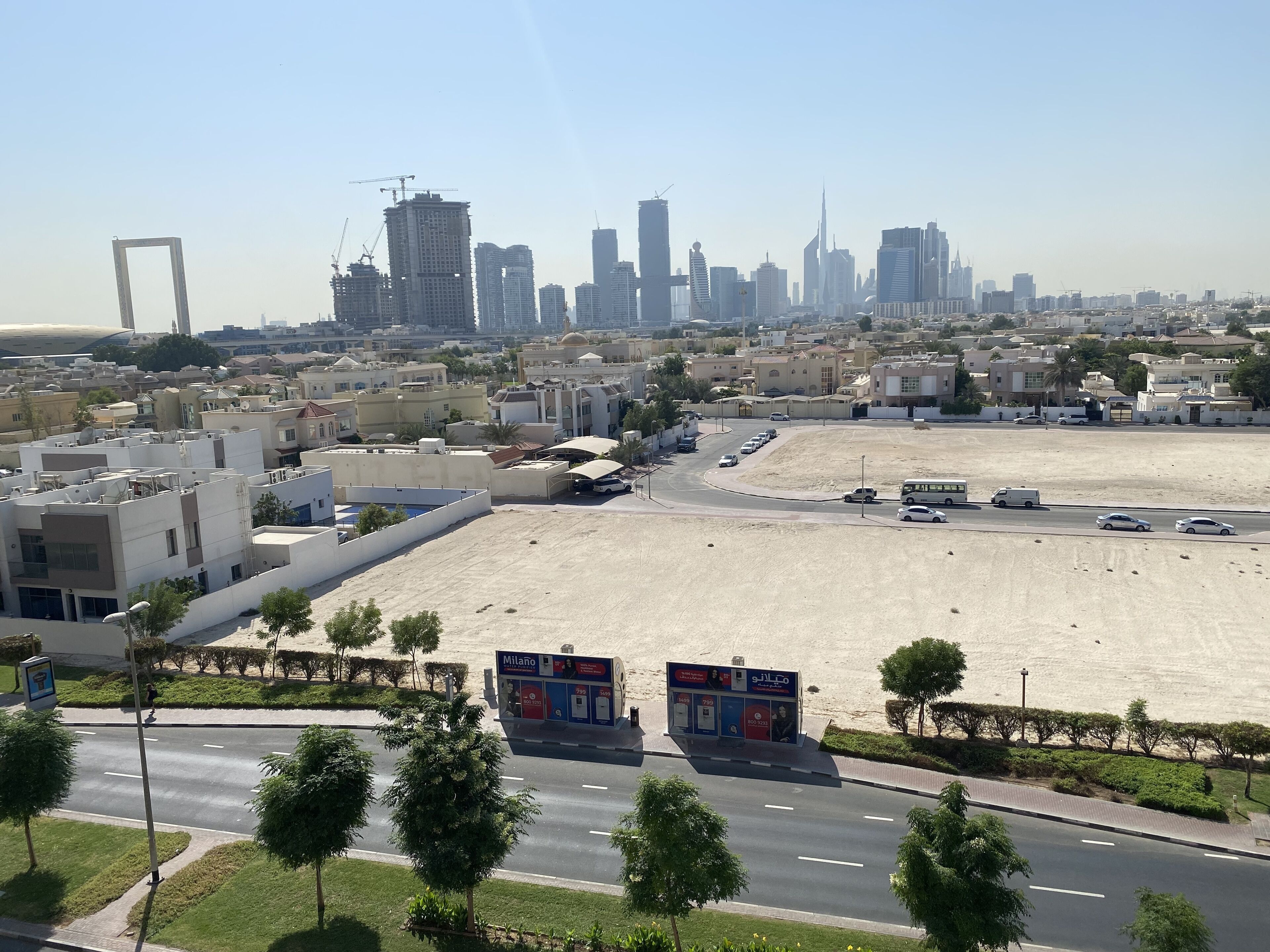 A cityscape with modern buildings, a large open parking area, and a clear sky.