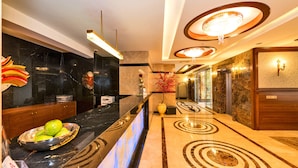 Un moderno vestíbulo de hotel con un mostrador de recepción de mármol, un jarrón grande con flores rojas y un piso con diseño.