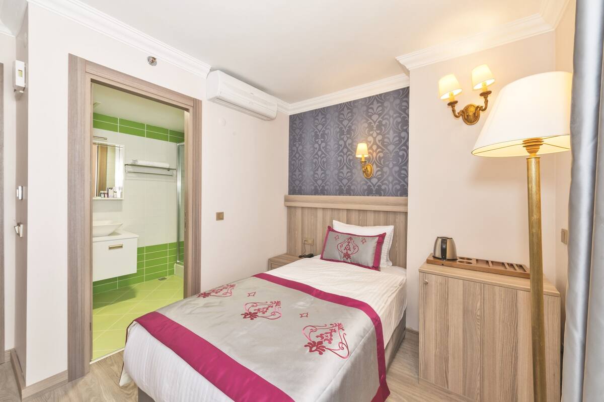 A hotel room with a bed, bedside table, lamp, and a view of the bathroom.