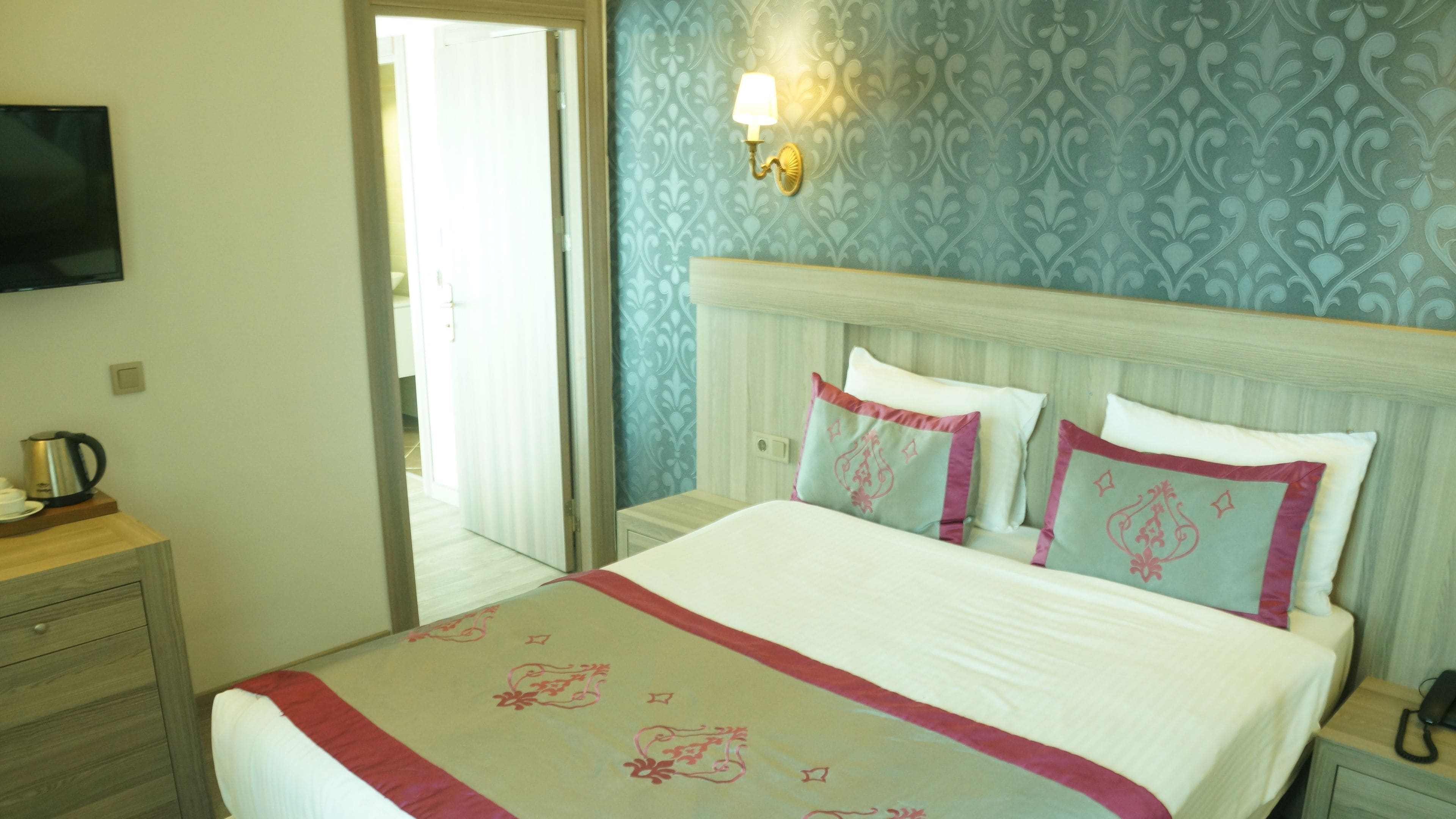 Habitación de hotel con cama, mesita de noche, televisión y puerta que da a un balcón.