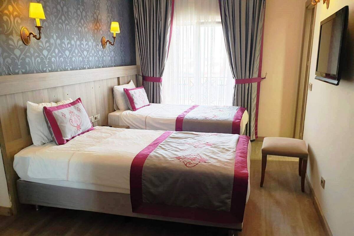 A hotel room with two beds, a bench, a TV, and patterned wallpaper.