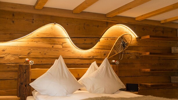 Un dormitorio tipo cabaña de madera con cabecera curvada, ropa de cama blanca y una mesita de noche con lámpara.