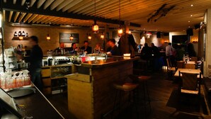 Zona de bar con vigas de madera, luces colgantes y una barra con diferentes botellas y vasos.