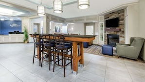 A spacious hotel lobby with a central island, bar stools, a flat-screen TV, and a fireplace. - Baymont by Wyndham Erie (Erie)