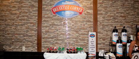 A breakfast bar area with a sign reading "Baymont Breakfast Corner," bottles of beverages, and a table with a white tablecloth.