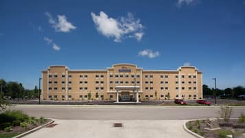 Um hotel grande, com vários andares, entrada central e estacionamento em frente.