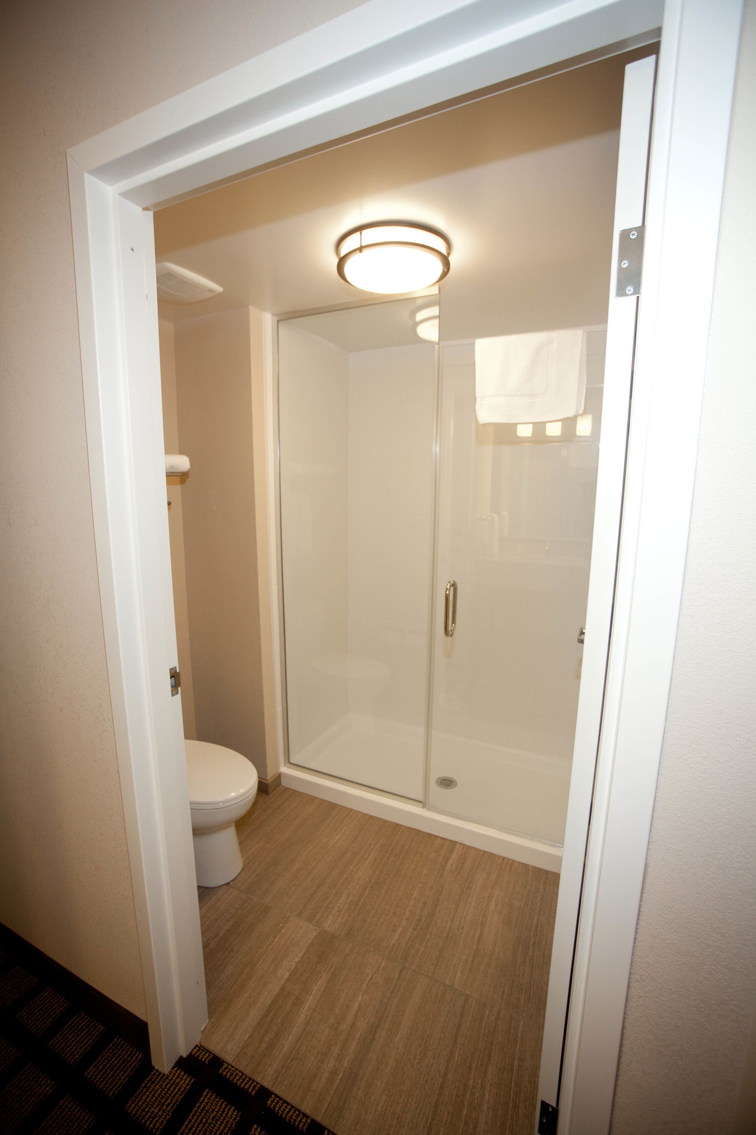 A bathroom with a toilet, a glass-enclosed shower, and a light fixture above the shower.