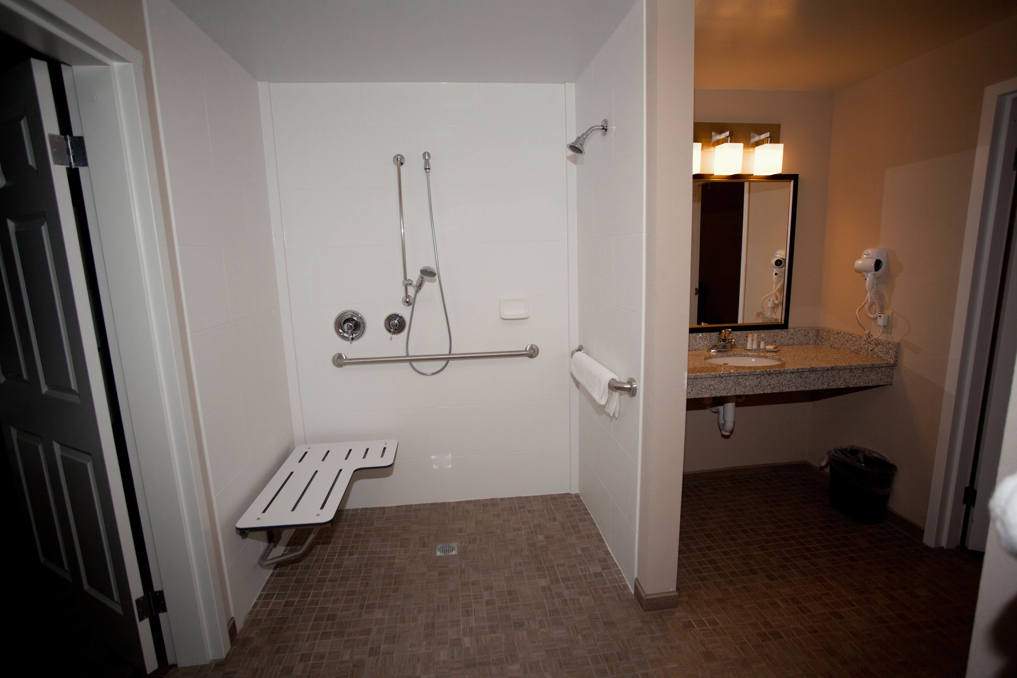 A bathroom with a shower, a hand dryer, a towel rack, and a sink.