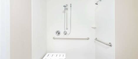 Un baño con ducha a ras de suelo, barras de apoyo y un banco blanco.