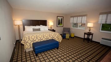 Une chambre d’hôtel comprenant un lit, deux tables de chevet avec des lampes, une chaise, une petite table et une fenêtre avec des stores.
