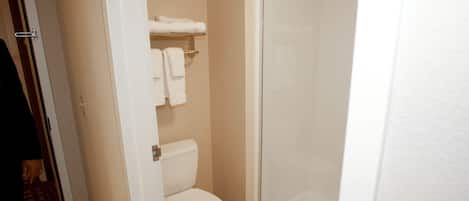 Une salle de bain d’hôtel équipée de toilettes, d’une douche à parois de verre et d’un porte-serviettes avec des serviettes.