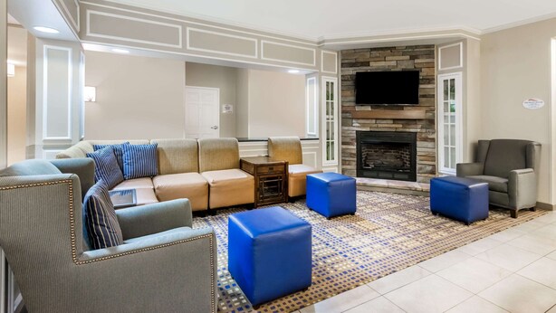 A living room with a sectional sofa, two ottomans, a fireplace, and a television mounted on the wall. - Baymont by Wyndham Erie (Erie)