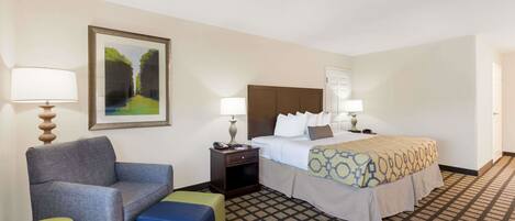 A hotel room with a bed, a chair, a nightstand, a lamp, and a painting on the wall.