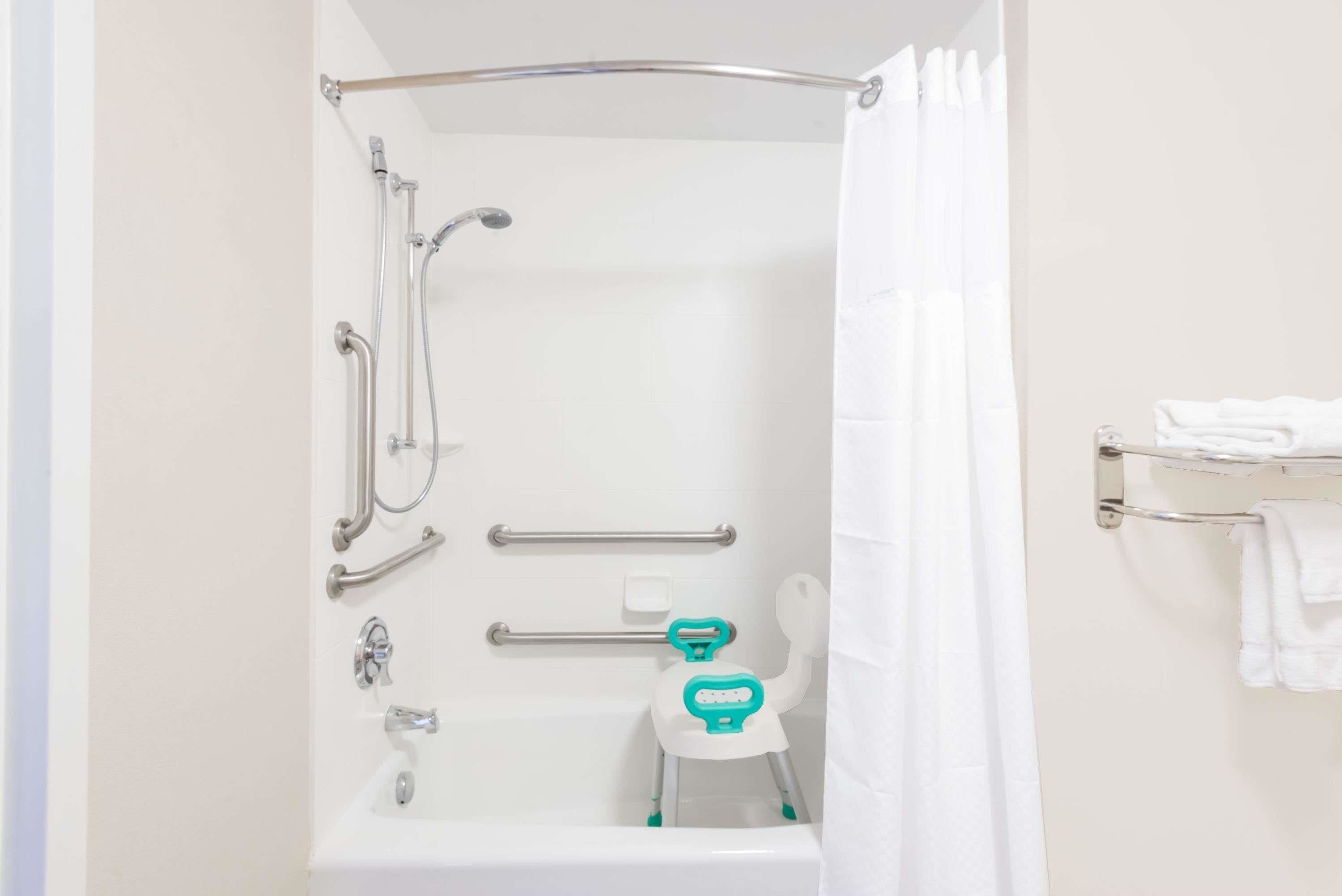 A bathroom with a bathtub, grab bars, a shower chair, and a towel rack.