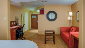 Una camera d'albergo con un letto, una scrivania, un divano rosso, un tavolino e una lampada.