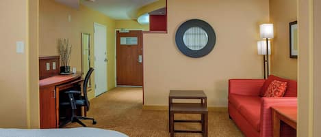 Una habitación de hotel con una cama, un escritorio, un sofá rojo, una mesita pequeña y una lámpara.