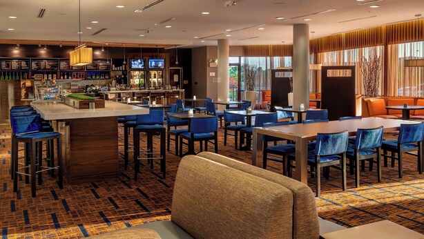 A hotel lobby with a bar area, seating arrangements, and a large window providing a view. - Courtyard Indianapolis Noblesville (Noblesville)