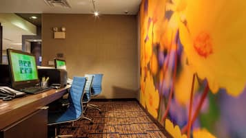 A hotel room with a desk, two monitors, a telephone, and a blue chair.