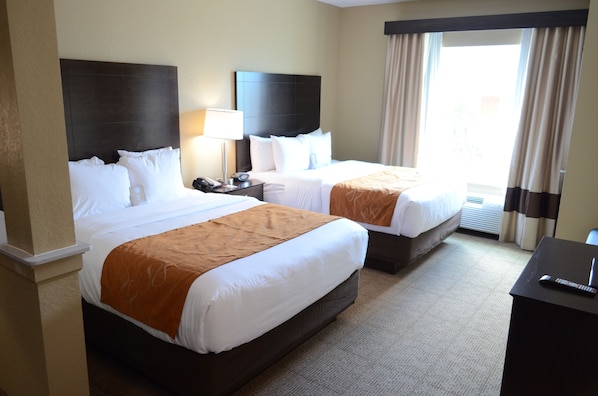 A hotel room with two beds, a nightstand, a lamp, and a view of the outdoors.