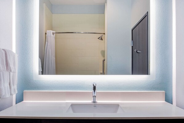A bathroom with a white sink, a mirror, and a shower area.