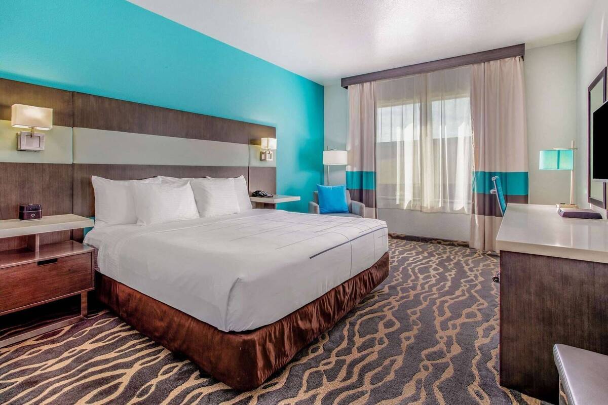 A hotel room with a large bed, a desk, a chair, a TV, and a window with curtains.