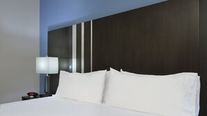 Un letto rifatto con lenzuola bianche, un comodino con una lampada e una testiera in legno scuro.