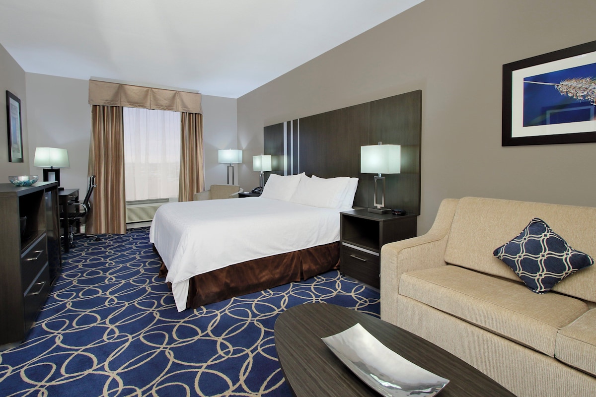 Habitación de hotel con una cama grande, un sofá, un escritorio y una lámpara.