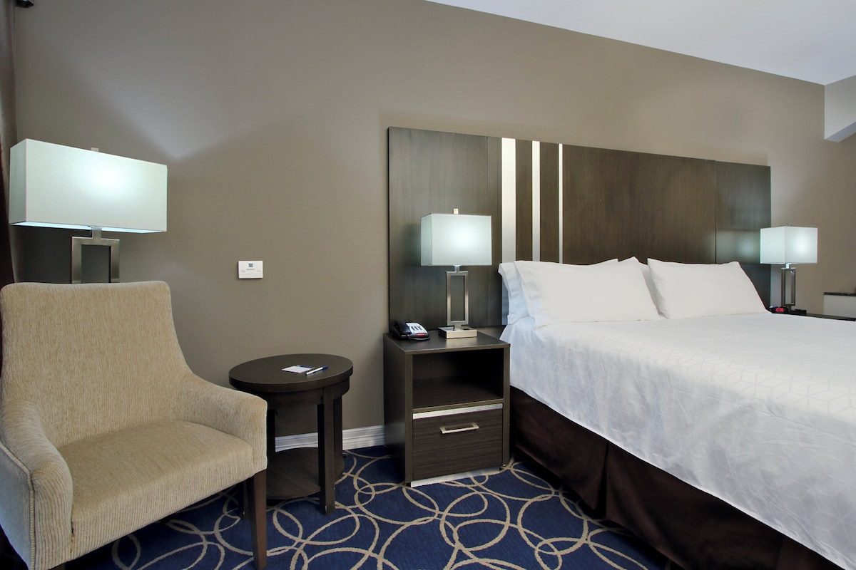 Una habitación de hotel con una cama, dos mesitas de noche, una silla y una pequeña mesa.