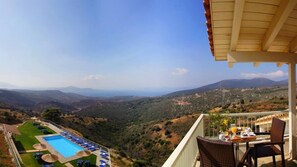 A balcony with a pool, lounge chairs, and a table with breakfast items. - Filion Eco Hotel (Karystos)