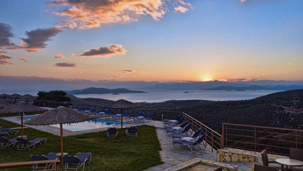 Un espace aménagé au bord de la piscine, avec des chaises longues et des parasols, offrant une vue sur une étendue d’eau et sur la terre ferme au loin.