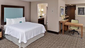 Habitación de hotel con una cama grande, un escritorio, una silla y un baño visible a través de una puerta abierta.