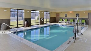 Una piscina con agua azul cristalina, una silla de salvavidas y una zona junto a la piscina con sillas y una puerta.