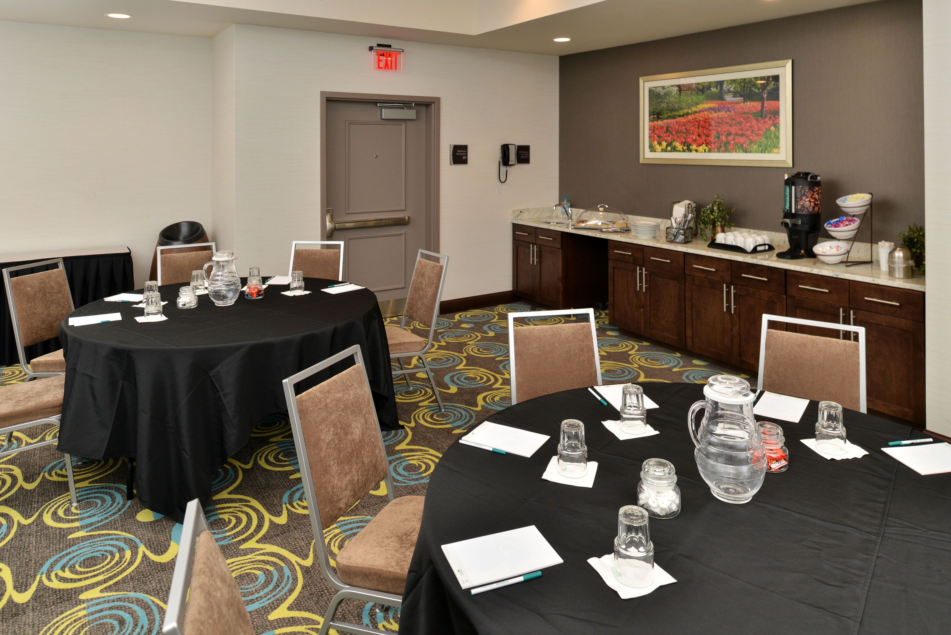 A conference room with a black table, chairs, a water pitcher, and a coffee station.