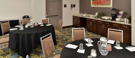 A conference room with a black table, chairs, a water pitcher, and a coffee station.