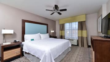 A hotel room with a bed, bedside tables, a desk, a television, and a ceiling fan.