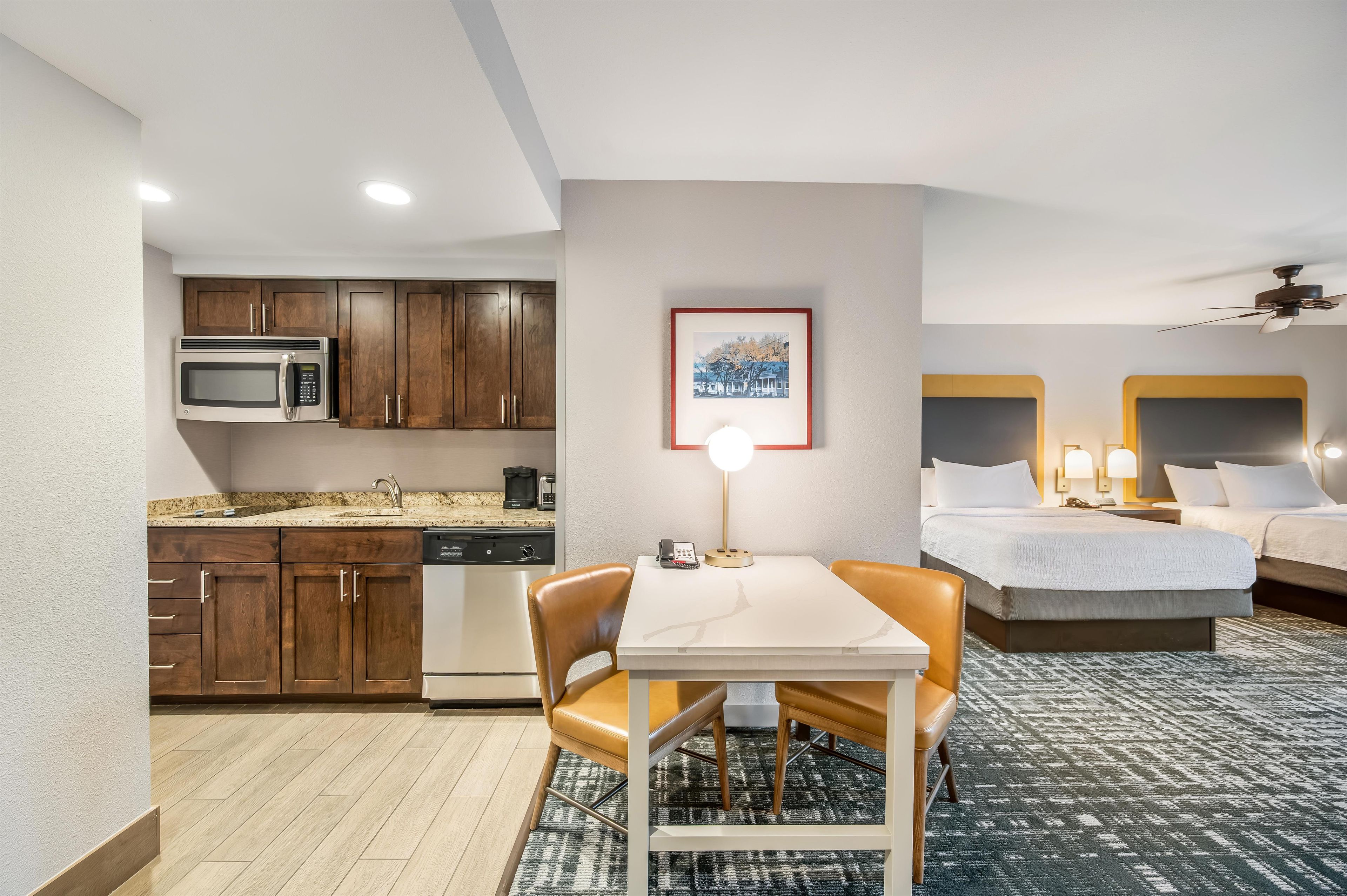 A compact hotel room with a kitchenette, a dining area, and a bed.