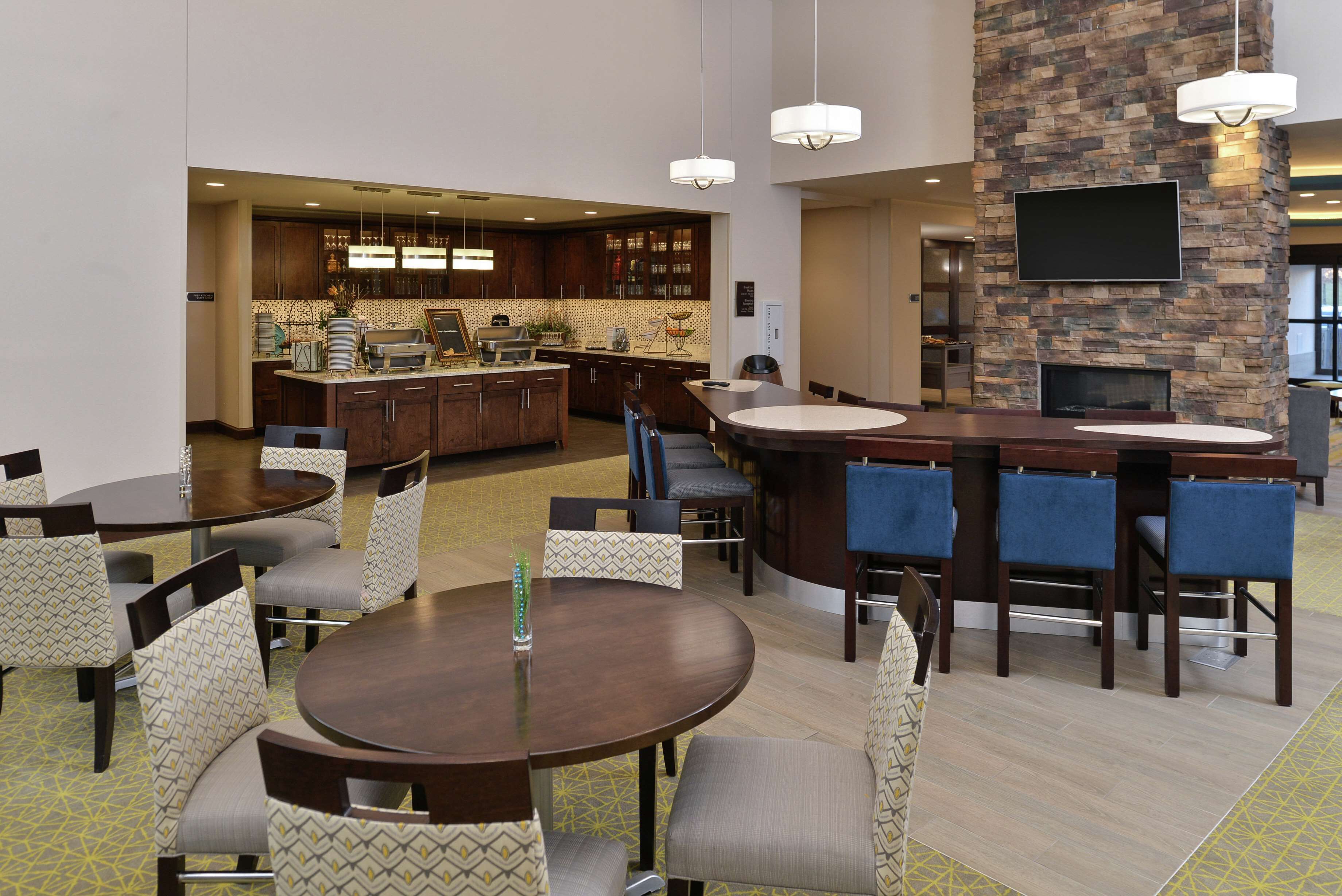 Un lobby de hotel moderno con una zona de bar central, mesas de comedor y una pared decorativa de piedra con un televisor de pantalla plana.