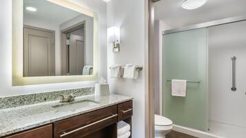 Een badkamer met een wastafel, spiegel, handdoekrek, toilet en een douchecabine met glazen wanden.